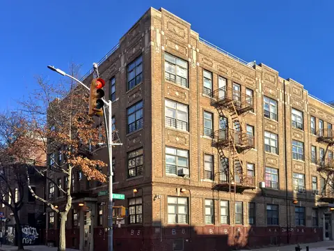 A tan brick New York apartment building with fire escapes on a street corner in Bedford-Stuyvesant, Brooklyn