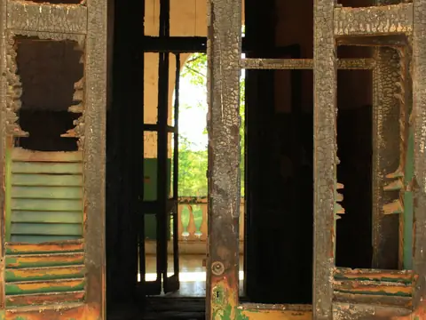 Charred door frames and a burned shutter in a fire-damaged building, daylight beyond