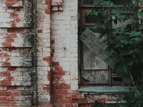 A window on an old brick building closed off with boards