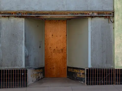 An empty storefront with plywood boarded across its entrance door
