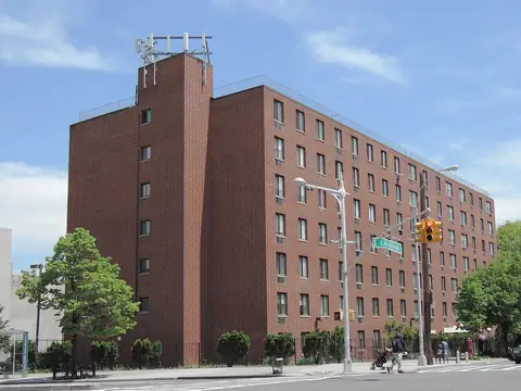 A tall red brick apartment building on a sunny Bronx street corner