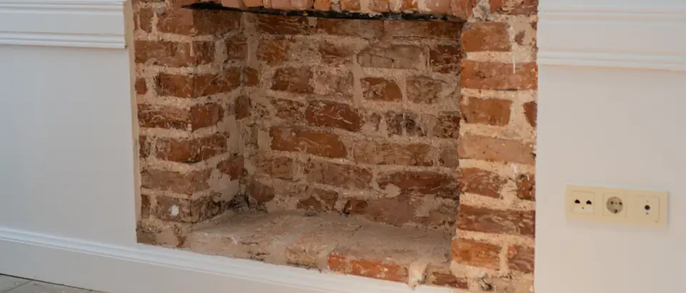 A bright, freshly painted empty room with a bare wood floor and an open brick fireplace