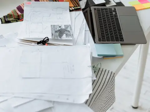 A laptop with piles of paper documents on a white table