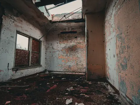 A damaged room with a broken ceiling, stained and peeling walls and debris on the floor