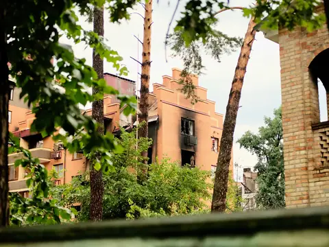 A brick apartment building with smoke-blackened windows on its upper floors, seen through trees