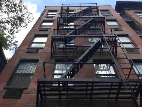 A red brick Manhattan apartment building with a black iron fire escape zigzagging down its front