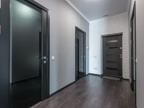 An apartment hallway with dark doors, gray walls and a wood floor