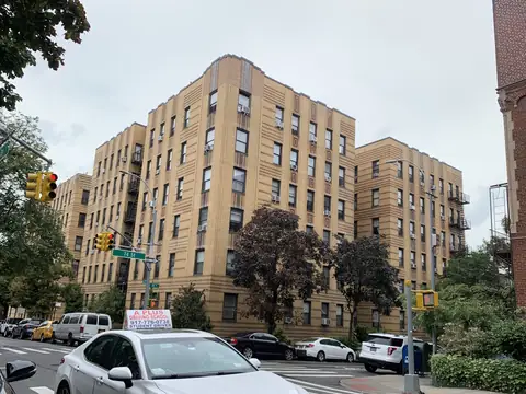 Tan brick apartment buildings on a tree-lined corner in Jackson Heights, Queens
