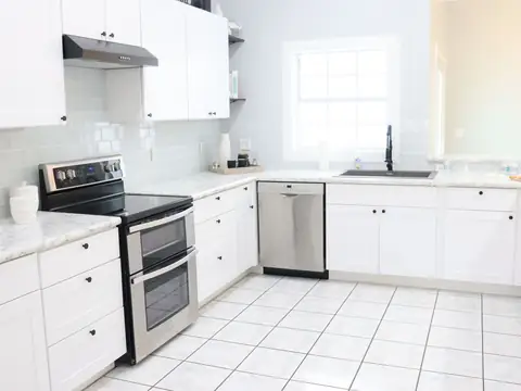 A bright kitchen with white cabinets, a stainless steel range and a white tile floor
