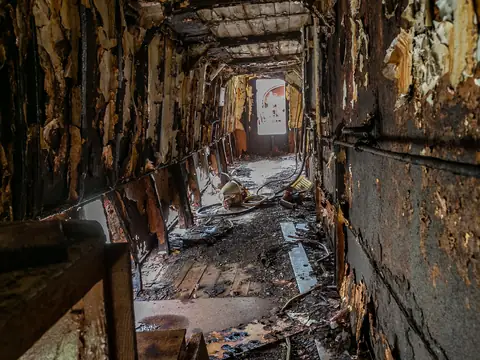 A fire-charred hallway with blistered, blackened walls and debris along the floor