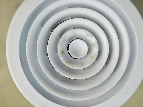 A round white ceiling air vent with dark stains around its center