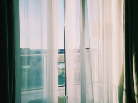 Sheer white curtains moving at an open balcony door in the sunlight