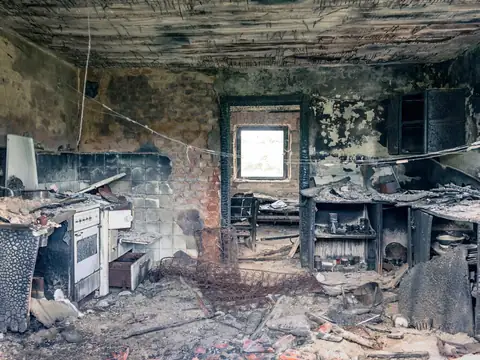 A burned kitchen with charred cabinets and soot-blackened walls, daylight at the window