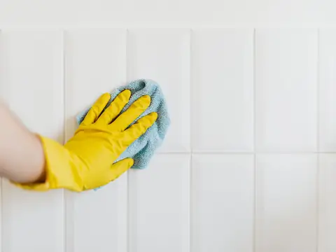 A gloved hand wiping a white wall with a cloth
