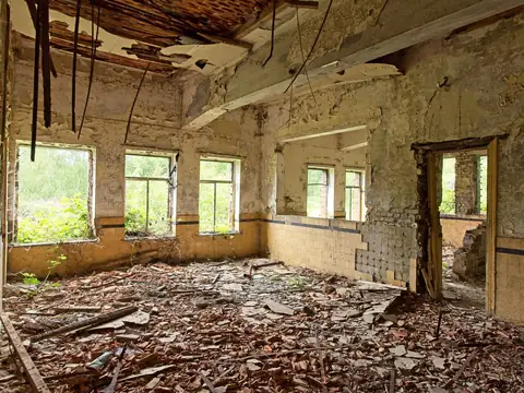 A damaged room with a broken ceiling and debris across the floor, daylight coming through the windows